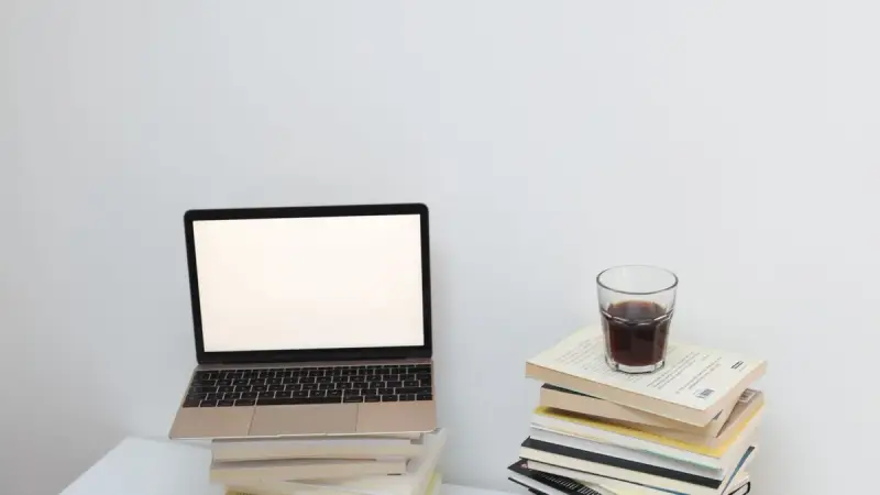 Portátil con pantalla vacía junto a libros y un vaso, sin personas